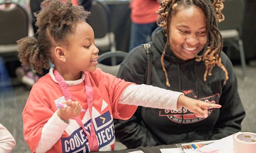 A young girl shows her computing project to a teacher.