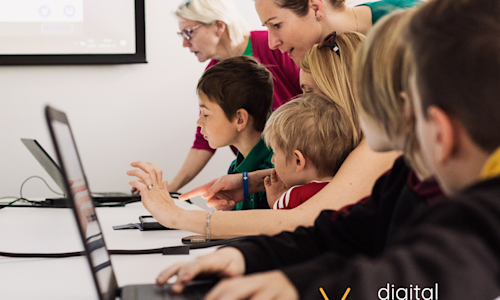 A picture of three young people coding on a laptop, being helped by their mentors.
