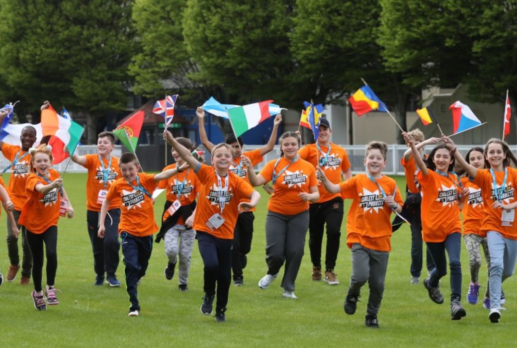 A group of children at a Coolest Projects event running across a field and waving flags of the world.