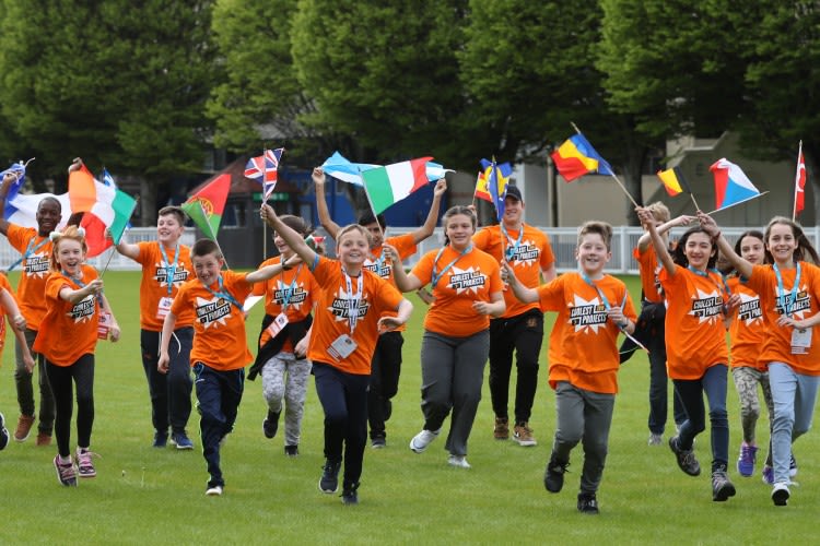 A group of children at a Coolest Projects event running across a field and waving flags of the world.