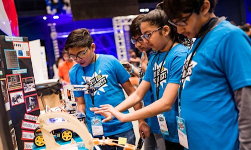 Four young people look at a robotic arm technology project.
