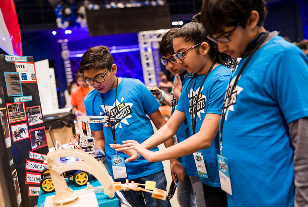 Four young people look at a robotic arm technology project.