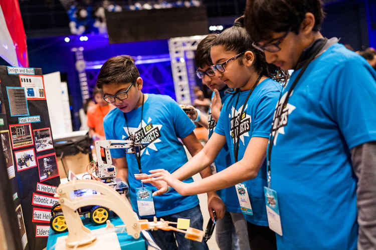 Four young people look at a robotic arm technology project.