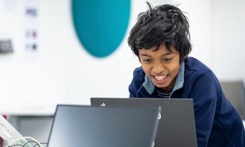 A young participant grinning as he uses a laptop at the Raspberry Pi Foundation headquarters
