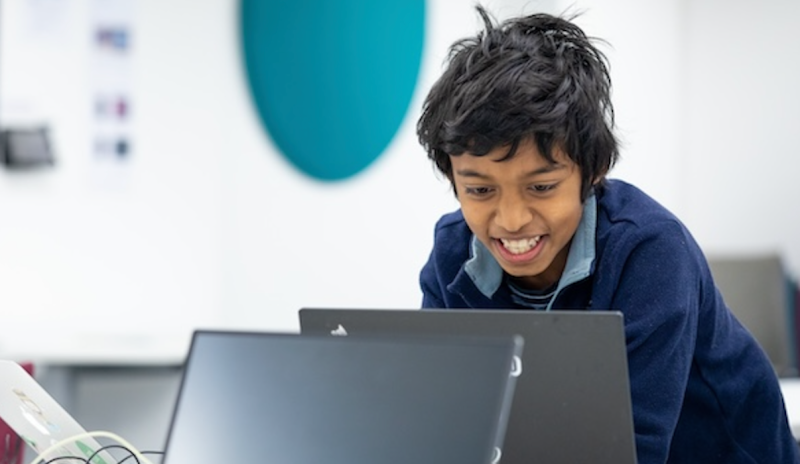 A young participant grinning as he uses a laptop at the Raspberry Pi Foundation headquarters