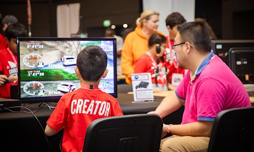 A young boy and a teacher play a computer game at an event.