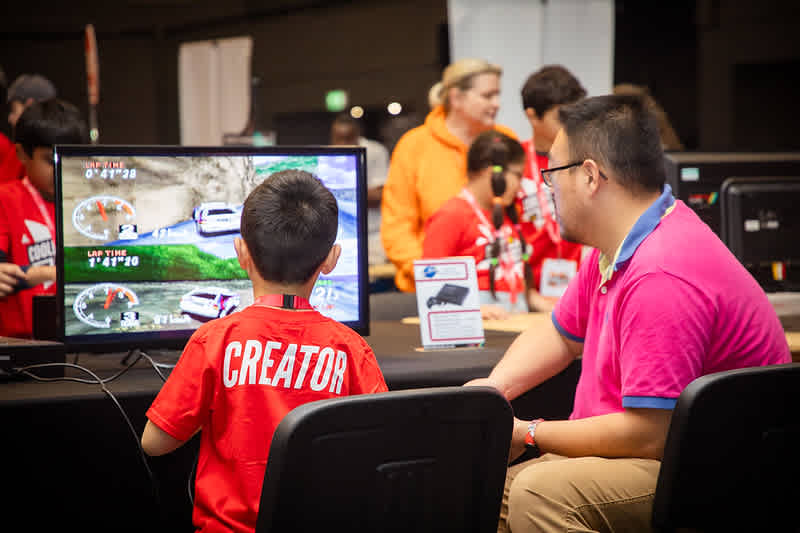 A young boy and a teacher play a computer game at an event.