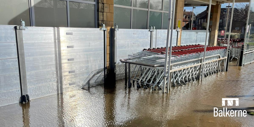 Shopping trolleys surrounded by flood water with shop flood defences behind them,