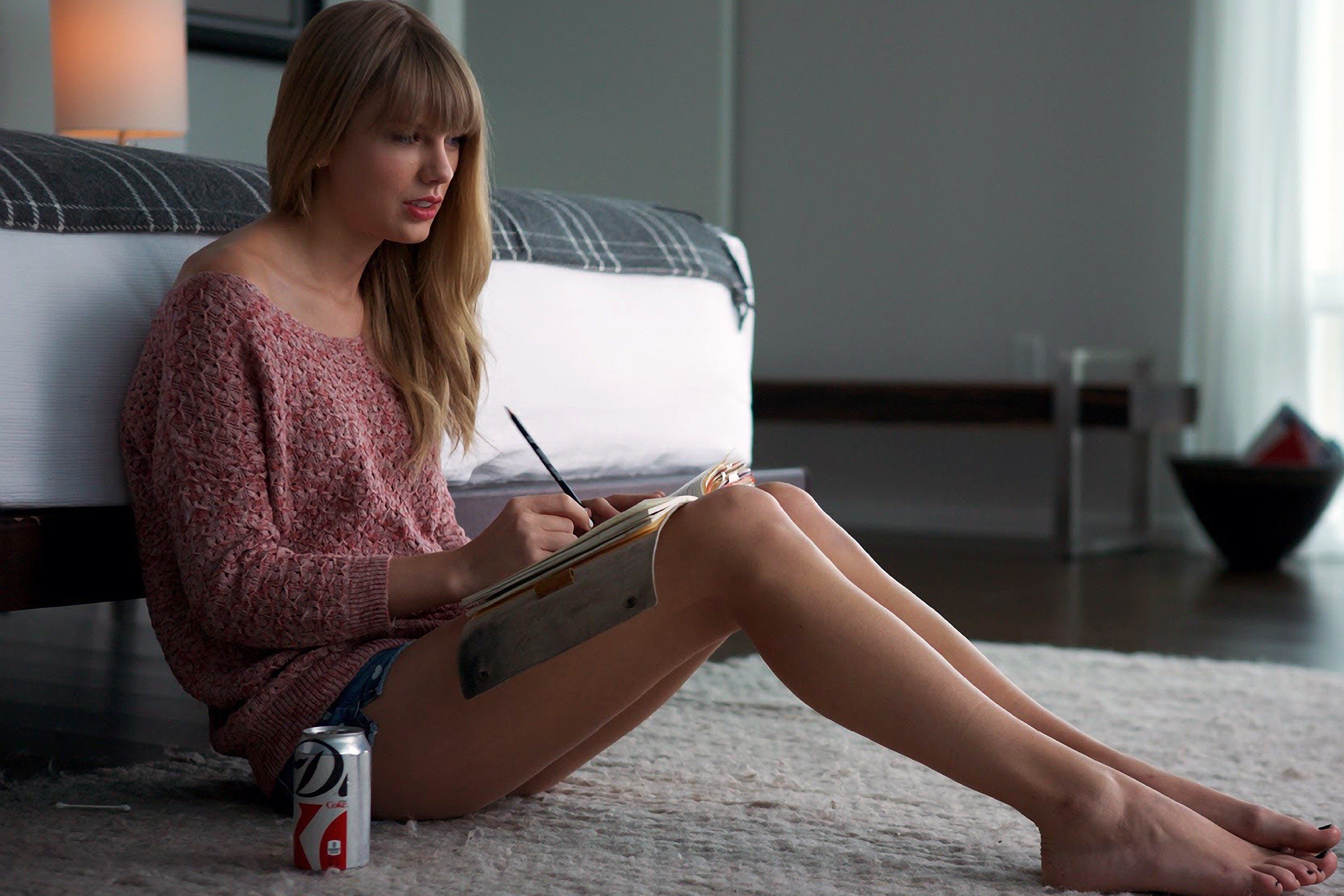 Taylor Swift sitting on the floor beside a bed.