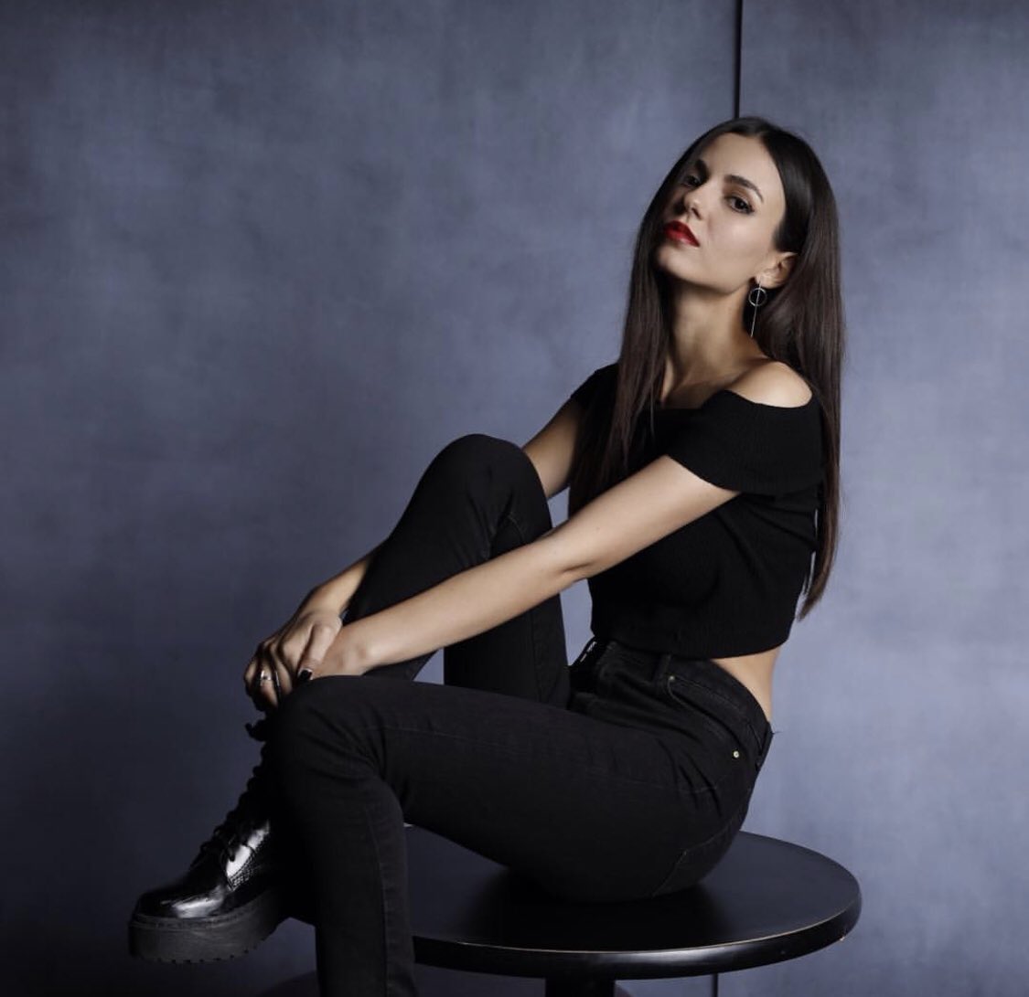 Victoria Justice sitting on a small round table wearing all black.