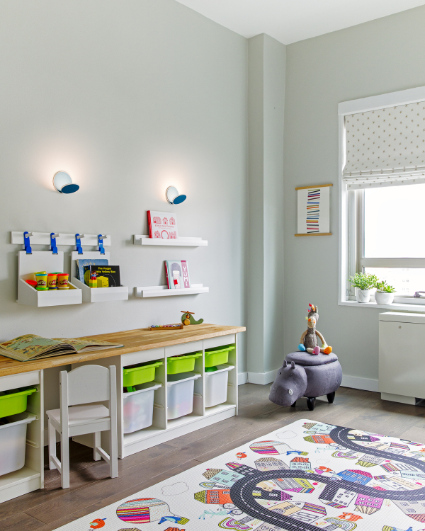 Lincoln Tower Apartment residential interior design renovation by Basicspace. Playful kids desk and wall storage with adjustable lighting. Art bins, baskets, shelving, and wall hooks for easy access to toys, arts and crafts, and books. Play mat and roman blackout shades complete the space.