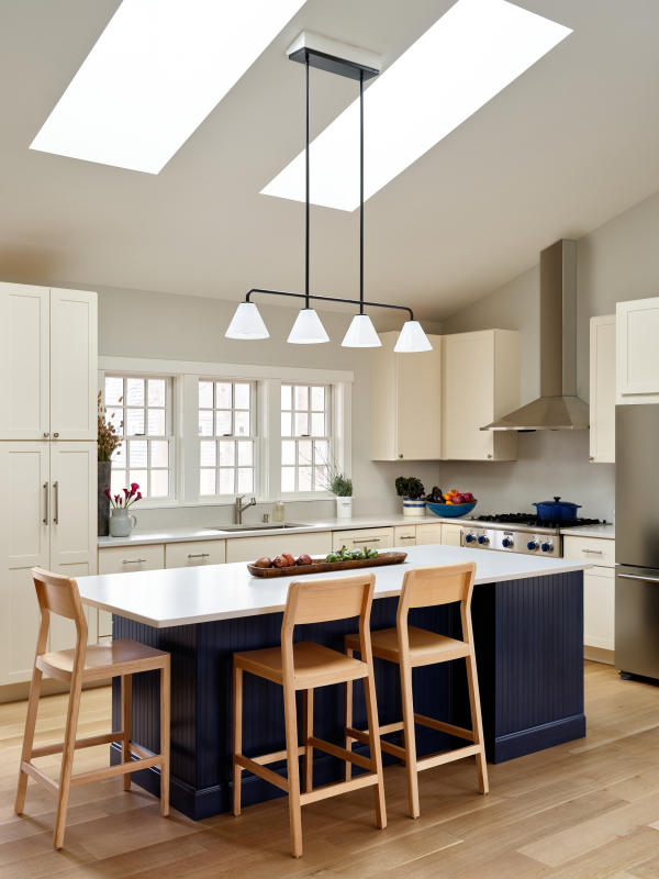 Two large skylights frame the kitchen island from above. The island features deep blue cabinets to compliment the natural tones of the rest of the room, and a light grey quartz counter.