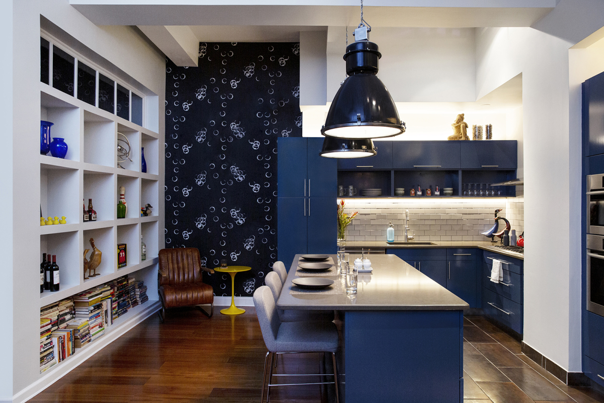 Hell's Kitchen Loft residential interior design by Basicspace. Bold glossy blue kitchen cabinets with white open display shelving, fun black wallpaper and oversized pendant lights. Counter stools at island.