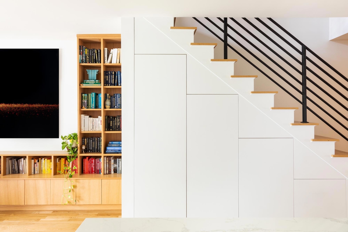 Jersey City Condo residential interior design by Basicspace. Contrast of white and wood alignment of storage elements. Under stair storage and open shelving with black metal stair banister.