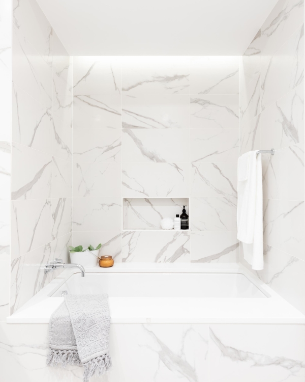 Jersey City Condo residential interior design by Basicspace. Bathroom tub nook with elegant porcelain marble tile clad on all surfaces, drop-in jacuzzi tub, and cove lighting.