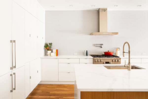 Jersey City Condo residential interior design by Basicspace. Clean white kitchen with subtle grey subway tile backsplash. Pot filler with hood above range, stainless steel sink, pull down faucet and quartz waterfall countertop island.