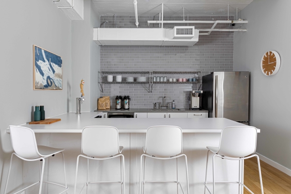 This kitchen space remained bright since it was interior to the windows and needed a facelift. Stools run along the island and there are prime amenities like cold-brew on tap and snack drawers, and hot coffee.