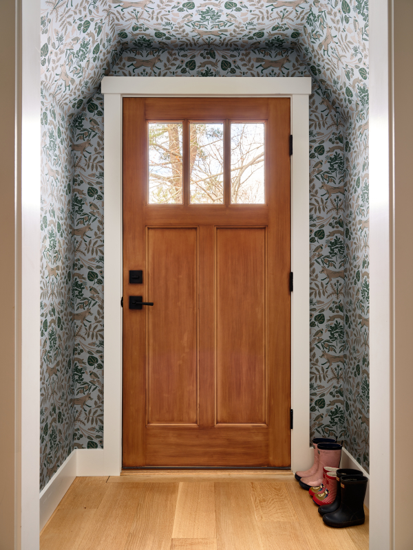 This Cape Elizabeth home's entrance is the perfect transition from the outdoors. wrapped completely in patterned wallpaper, a solid wood door with a paneled glass door.