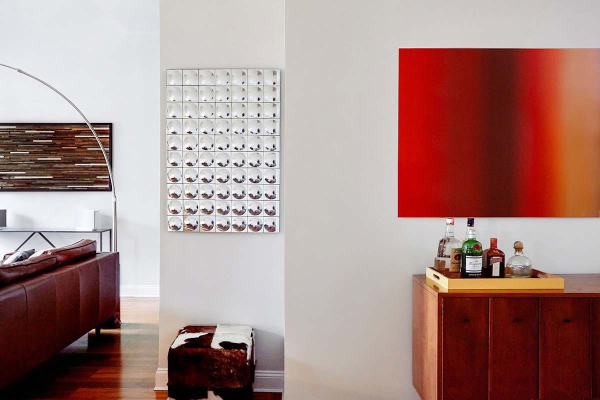 Hell's Kitchen Loft residential interior design by Basicspace. Wood, mirror and ombre orange artwork throughout the apartment. Cow hide ottoman and leather sofa.