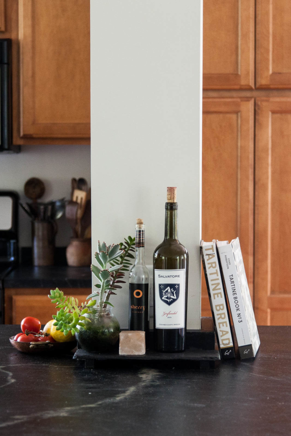 Jerusalem Road House residential interior design by Basicspace. Lifestyle detail shot of items displayed within the kitchen. Olive oil, baking books, and fresh fruit and succulent plants on top of black soapstone countertops.
