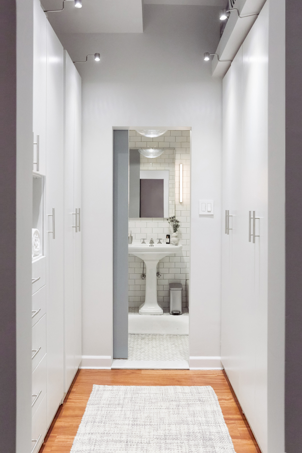 Hell's Kitchen Loft residential interior design by Basicspace. View through wardrobe into bathroom with barn sliding door. White minimal build-in closet millwork.