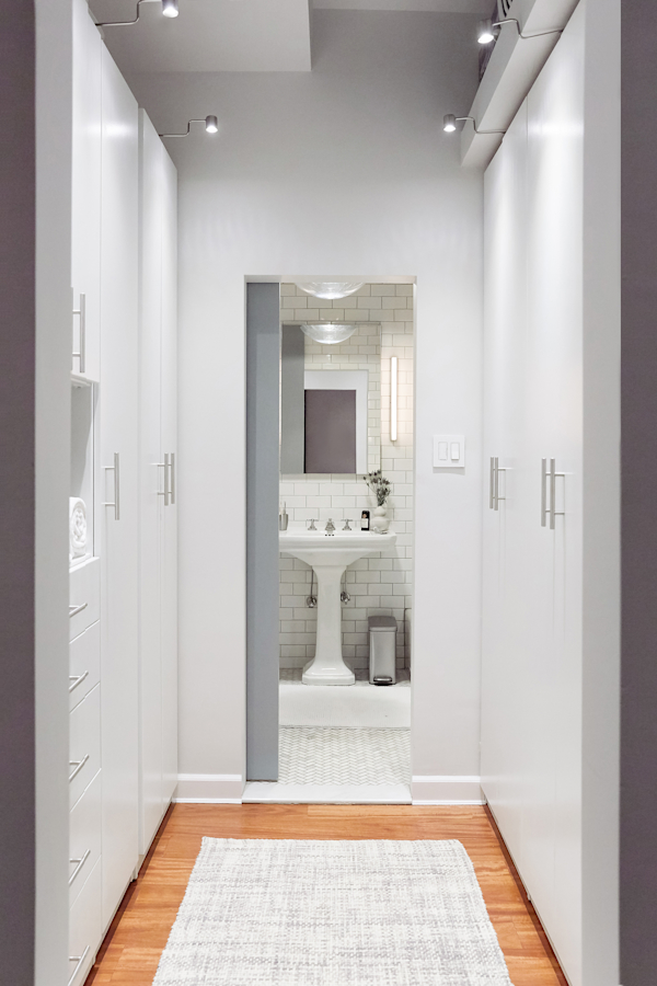 Hell's Kitchen Loft residential interior design by Basicspace. View through wardrobe into bathroom with barn sliding door. White minimal build-in closet millwork.