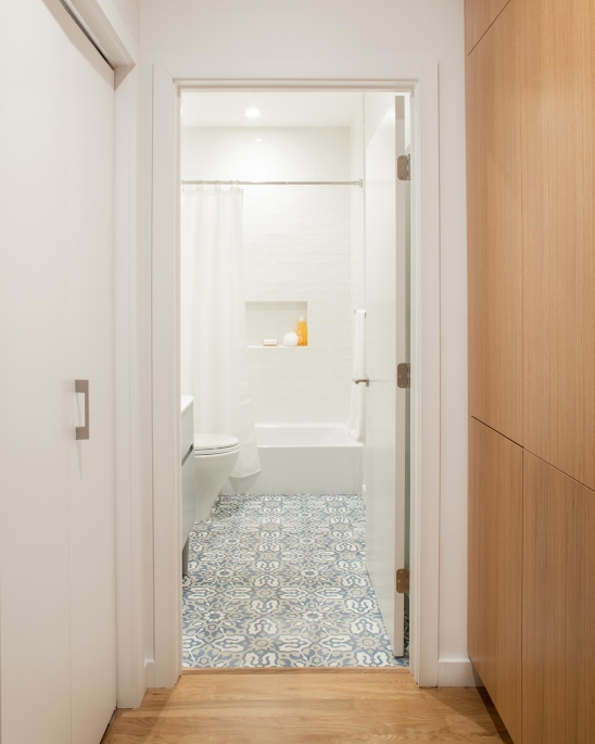 Jersey City Condo residential interior design by Basicspace. Kid's bathroom with concrete tile flooring and white subway tile. Build-in laundry room wood paneling doors.