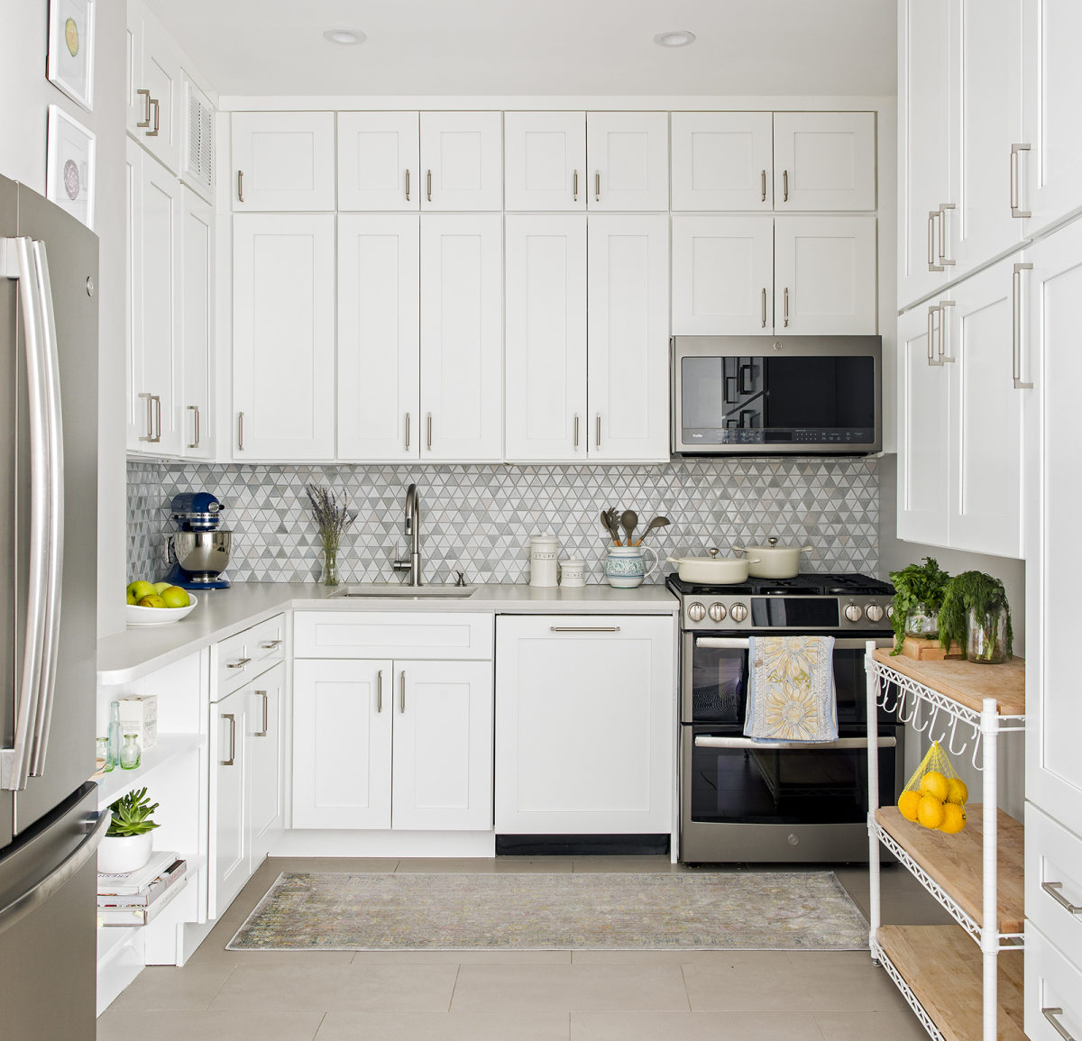 Lincoln Tower Apartment residential interior design renovation by Basicspace. White kitchen cabinetry with mosaic backsplash, light grey counters and matte slate appliances and butcher block cart.