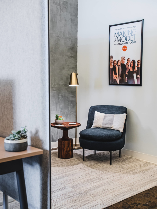 Hudson Media office interior design renovation by Basicspace. Concrete textured paint with clean navy blue lounge chairs and wood block table. Carpet tile and felt acoustical panels divide the space.