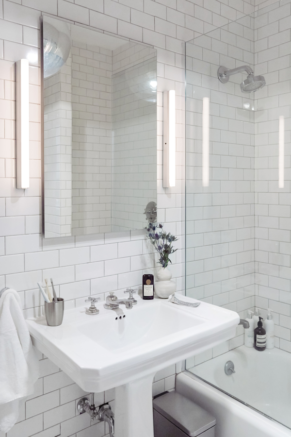 Hell's Kitchen Loft residential interior design by Basicspace. Bathroom with white subway tile, pedestal sink, medicine cabinet and fixed glass panel on tub.
