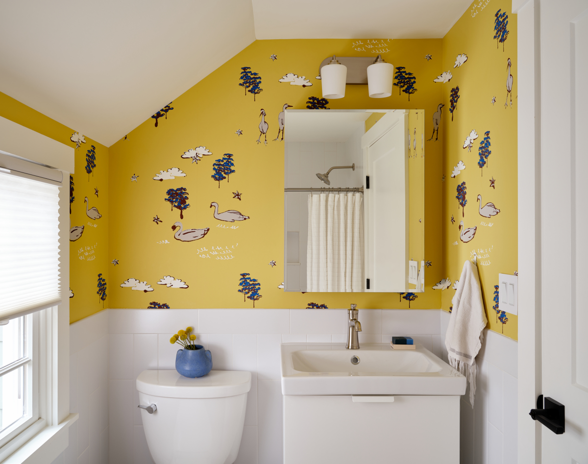 Playful and bright yellow patterned wallpaper adds character to this children's bathroom. A white half wall tile wraps the room, framing the vanity.