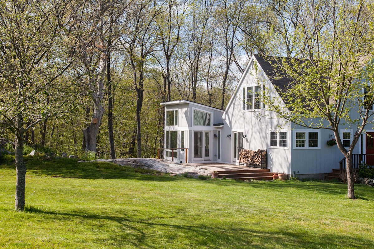 Jerusalem Road House residential interior design by Basicspace. Exterior view of the patio and addition into the family bonus room. Barn board siding of this farmhouse sits on lush green grass.