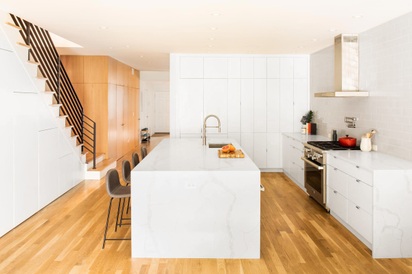 Jersey City Condo residential interior design by Basicspace. White kitchen, open stair, wood flooring with wood wall paneling. Pot filler with hood above range, stainless steel sink, pull down faucet and quartz waterfall countertop island.