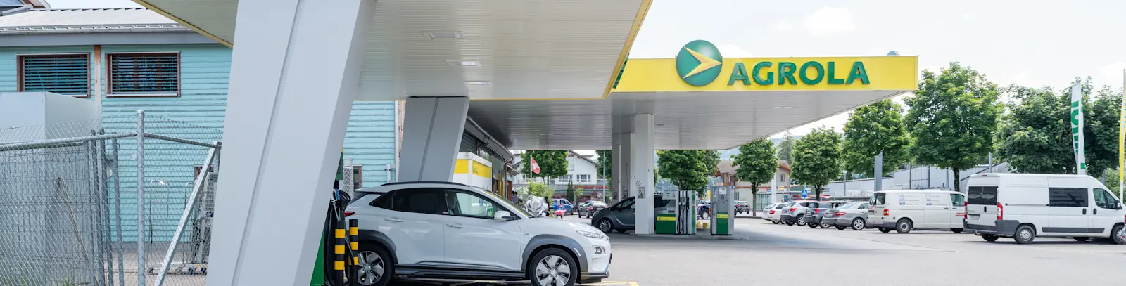 Auto an AGROLA Schnellladestation vor einer AGROLA Tankstelle mit Parkplatz.