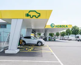 Voiture à la station de recharge rapide AGROLA devant une station-service AGROLA avec parking.