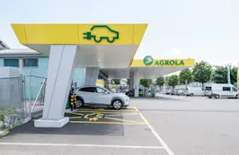 Auto an AGROLA Schnellladestation vor einer AGROLA Tankstelle mit Parkplatz.