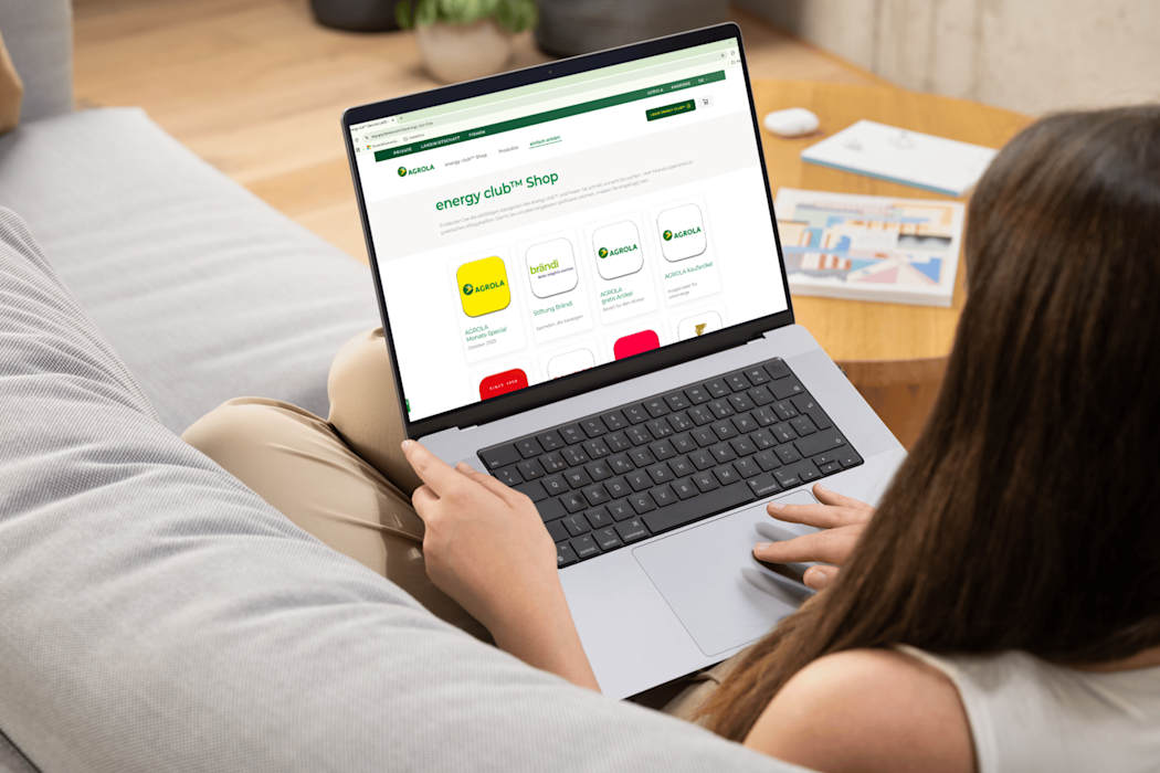 Person nutzt Laptop auf Sofa mit geöffnetem Agrola energy club Shop, der verschiedene App-Optionen anzeigt.