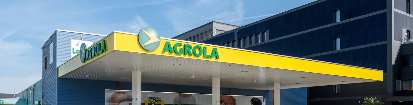 Photo de LANDI KoWy avec bande de toit de la station-service et façade recouverte de PV. Dans le ciel, des traînées de condensation d'avions