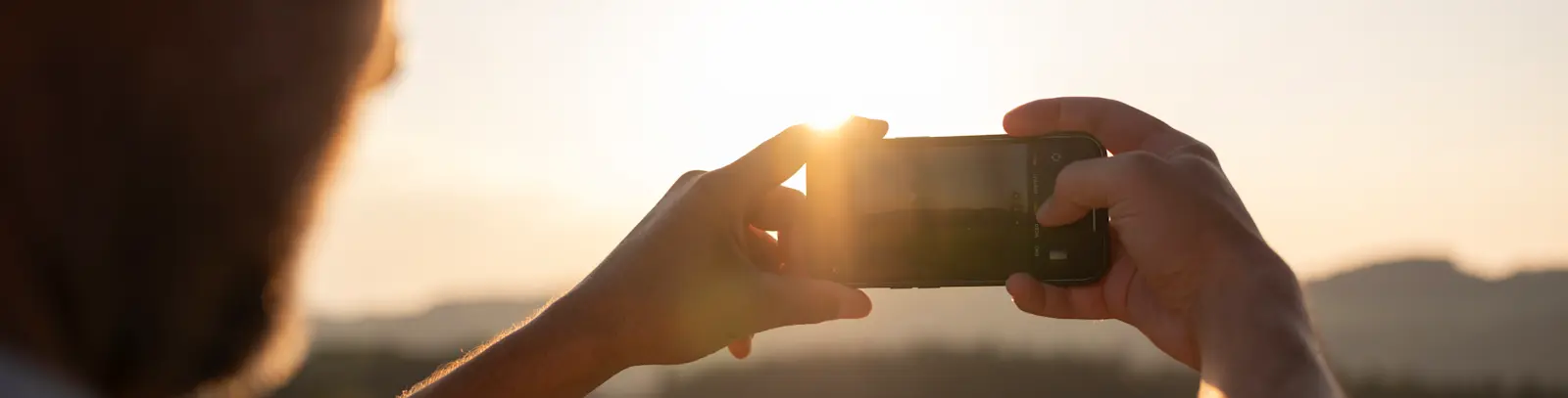 Smartphone au centre de l'image, avec derrière le soleil à l'horizon et un paysage verdoyant