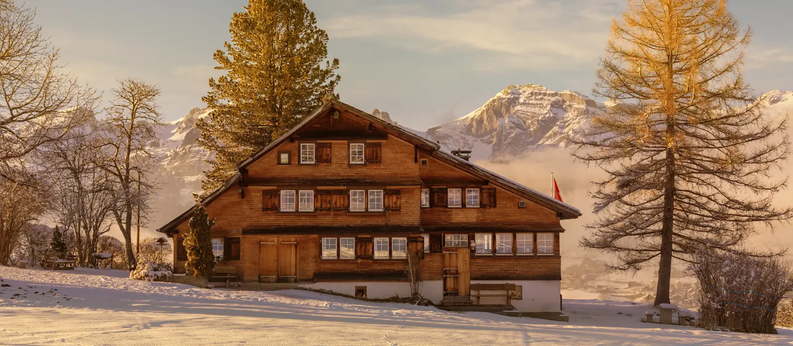 Traditionelles Schweizer Chalet im Winterlicht mit schneebedecktem Vordergrund und majestätischen Alpen im Hintergrund.