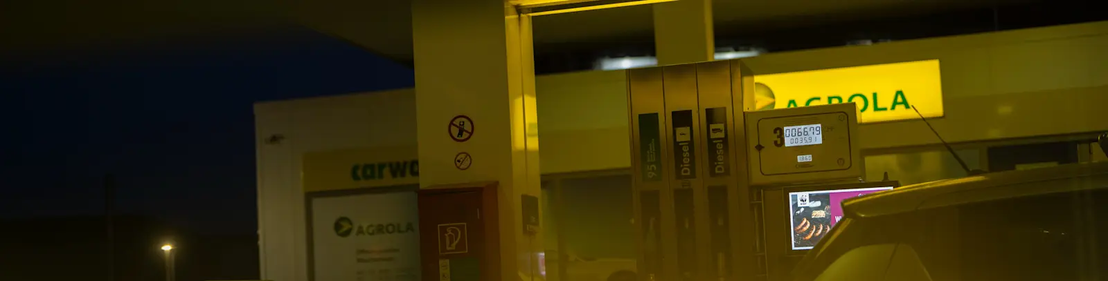 Vue d'une colonne de station-service AGROLA - éclairée avec les pistolets de distribution visibles.