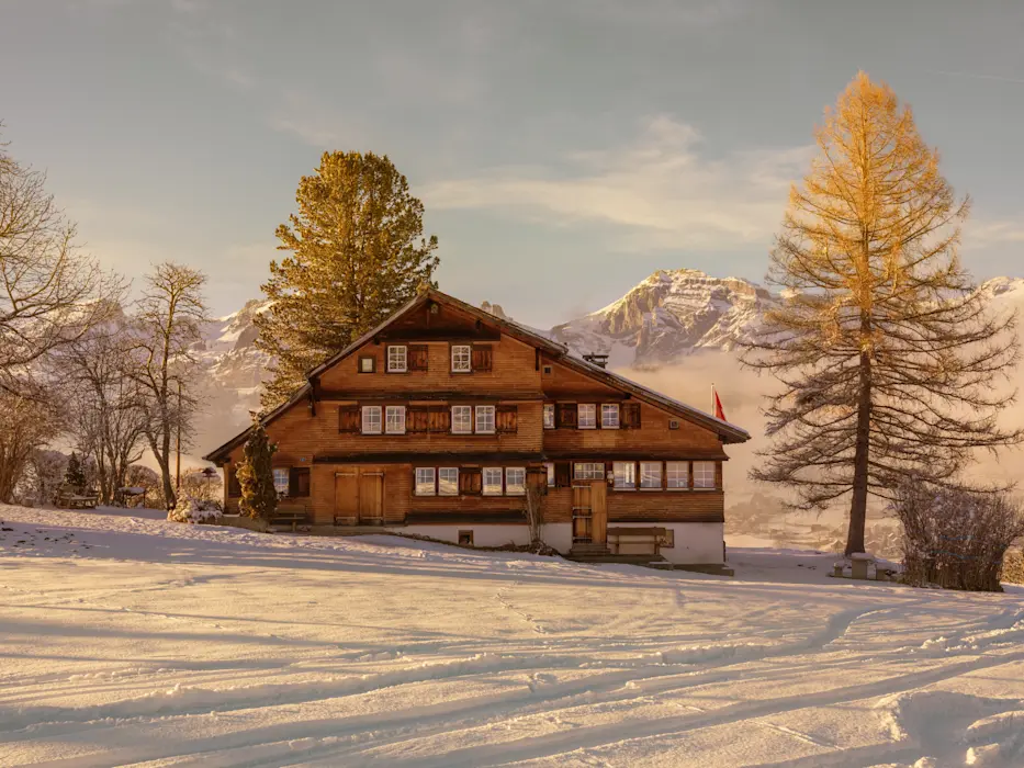 Traditionelles Schweizer Chalet im Winterlicht mit schneebedecktem Vordergrund und majestätischen Alpen im Hintergrund.