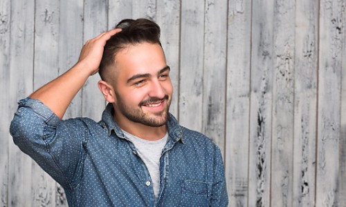 Smiling man rubs hand through his new hair following his hair transplant surgery.