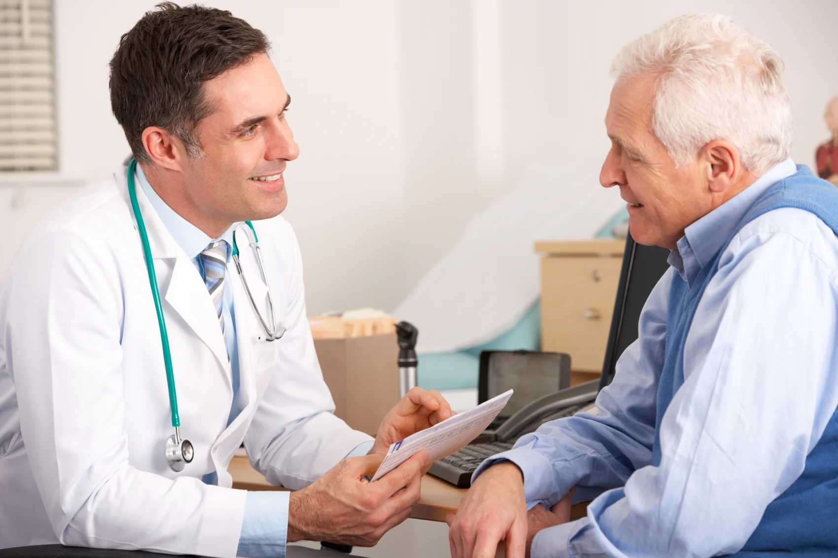Lächelnder Arzt im Gespräch mit einem älteren Mann während einer onkologischen Sprechstunde.