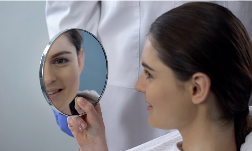 Woman looking in the mirror after undergoing rhinoplasty surgery.