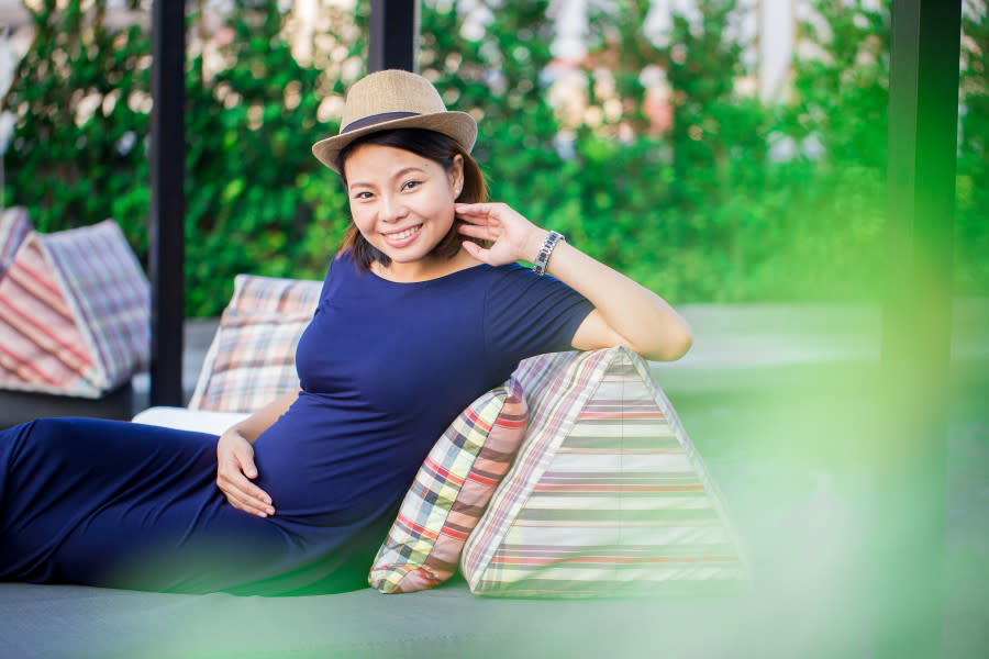 Pregnant woman sitting on bench smiling.