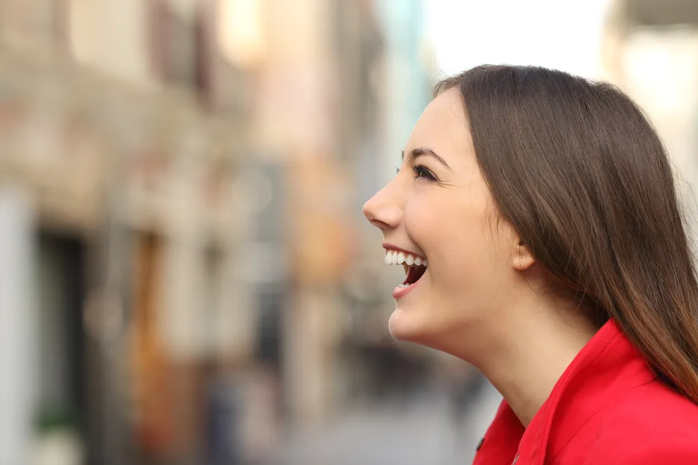 Happy, smiling woman laughing in the street with a blurred, urban background.