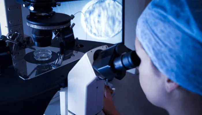 A lab technician performs an IVF procedure under a microscope.