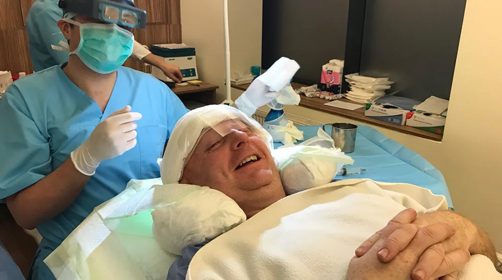 Patient liegt auf Behandlungsliege und lächelt während der Vorbereitung seiner FUE Haartransplantation.