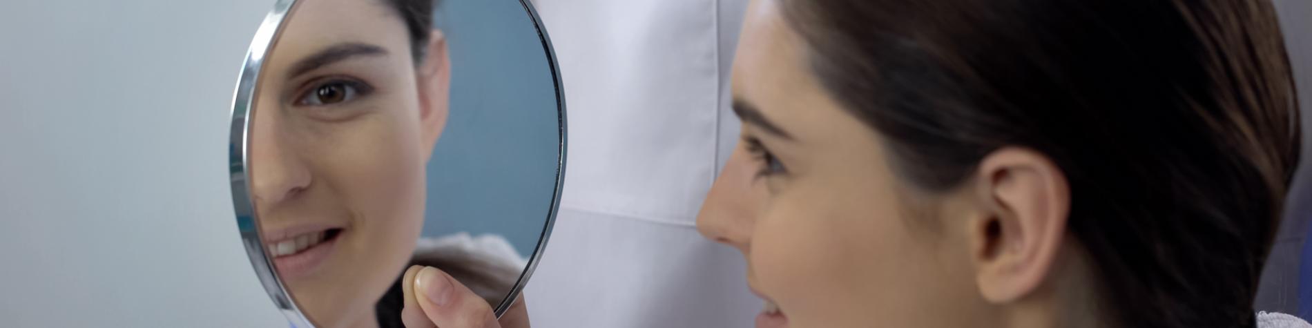 Woman looking in the mirror after undergoing rhinoplasty surgery.